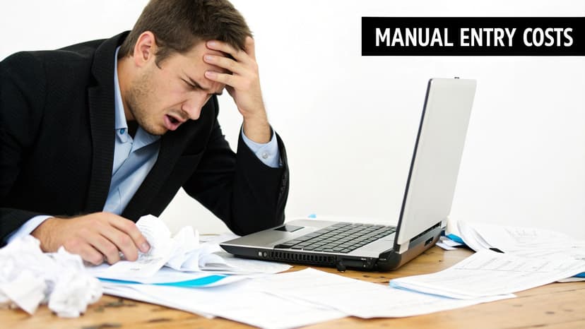 Stressed man overwhelmed by paperwork and a laptop, highlighting manual data entry costs.