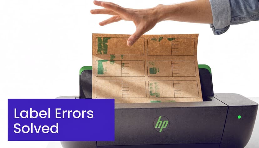A hand placing a sheet of printed address labels into a Hewlett-Packard printer with green ink smudges.