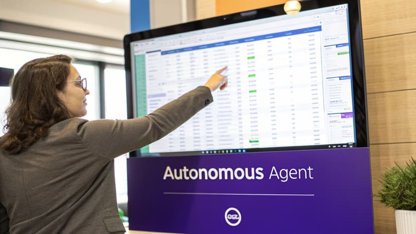 A woman in glasses points at a large screen displaying data and 'Autonomous Agent' text.